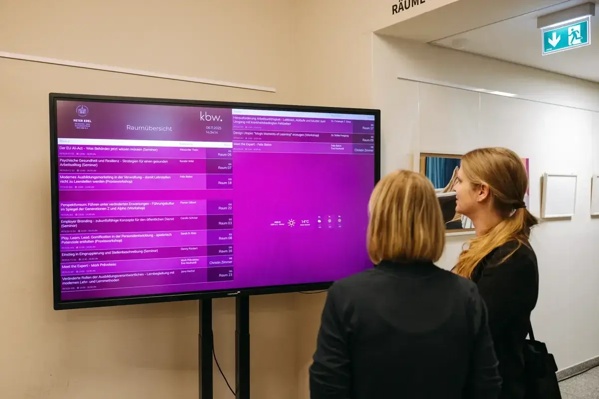 Teilnehmende schauen sich den digitalen Seminarplan im Foyer an