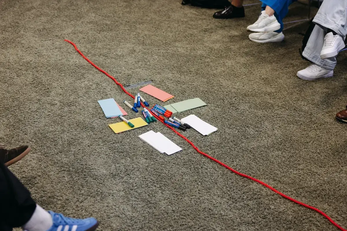Stillleben aus einem Workshop - eine rote Schnur trennt die Gruppen, in der Mitte liegen Seminar-Utensilien